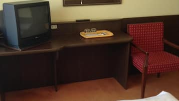 A hotel room with a bed, a desk with a television, a chair, and a mirror.