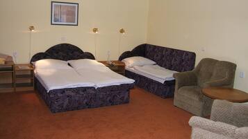 A room with two beds, a chair, a small table, and a framed picture on the wall.
