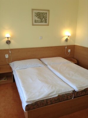 Uma cama de casal com roupa de cama branca, duas luminárias fixadas na parede e um quadro enquadrado na parede.