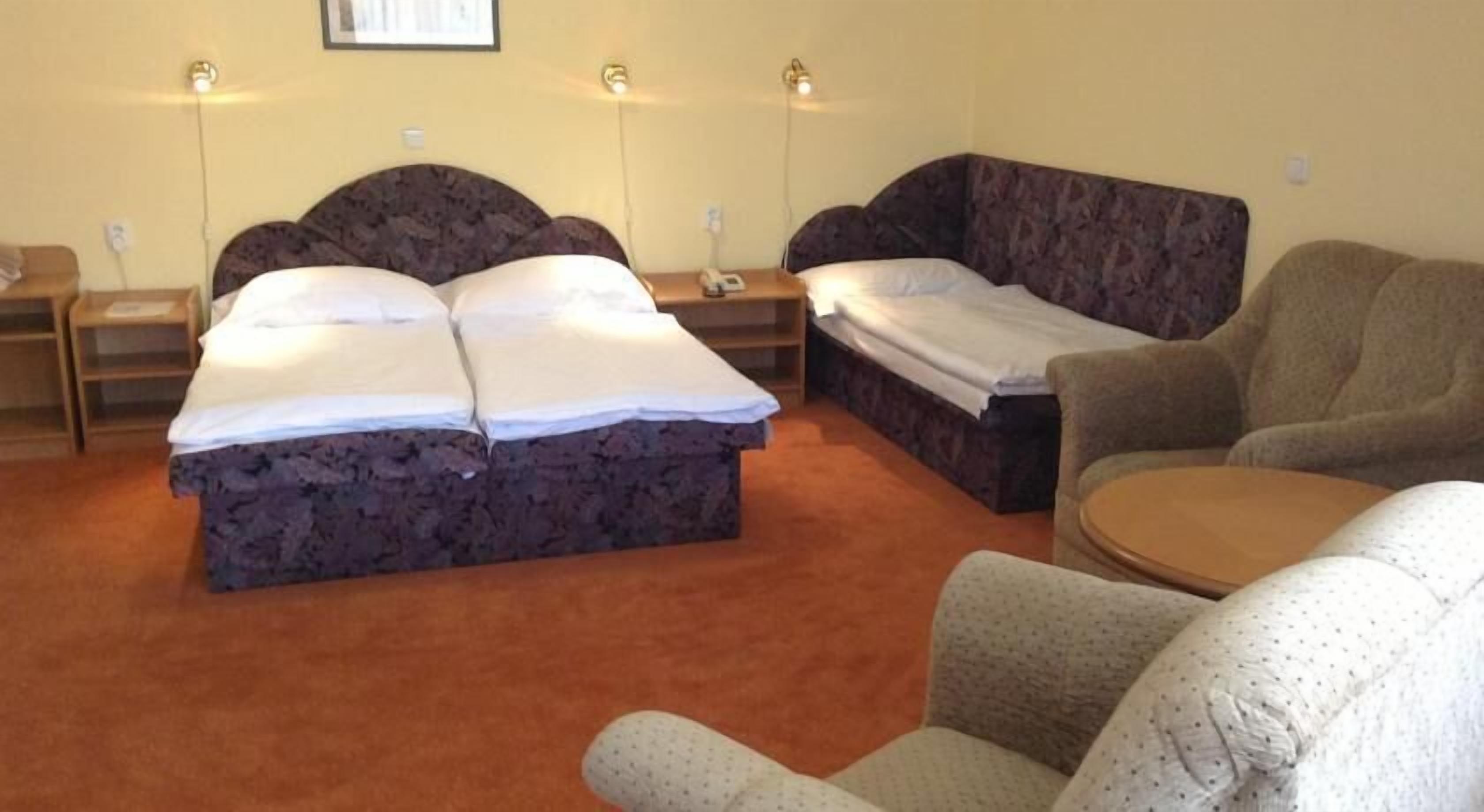 A hotel room with a large bed, a sofa, a chair, and a small table.