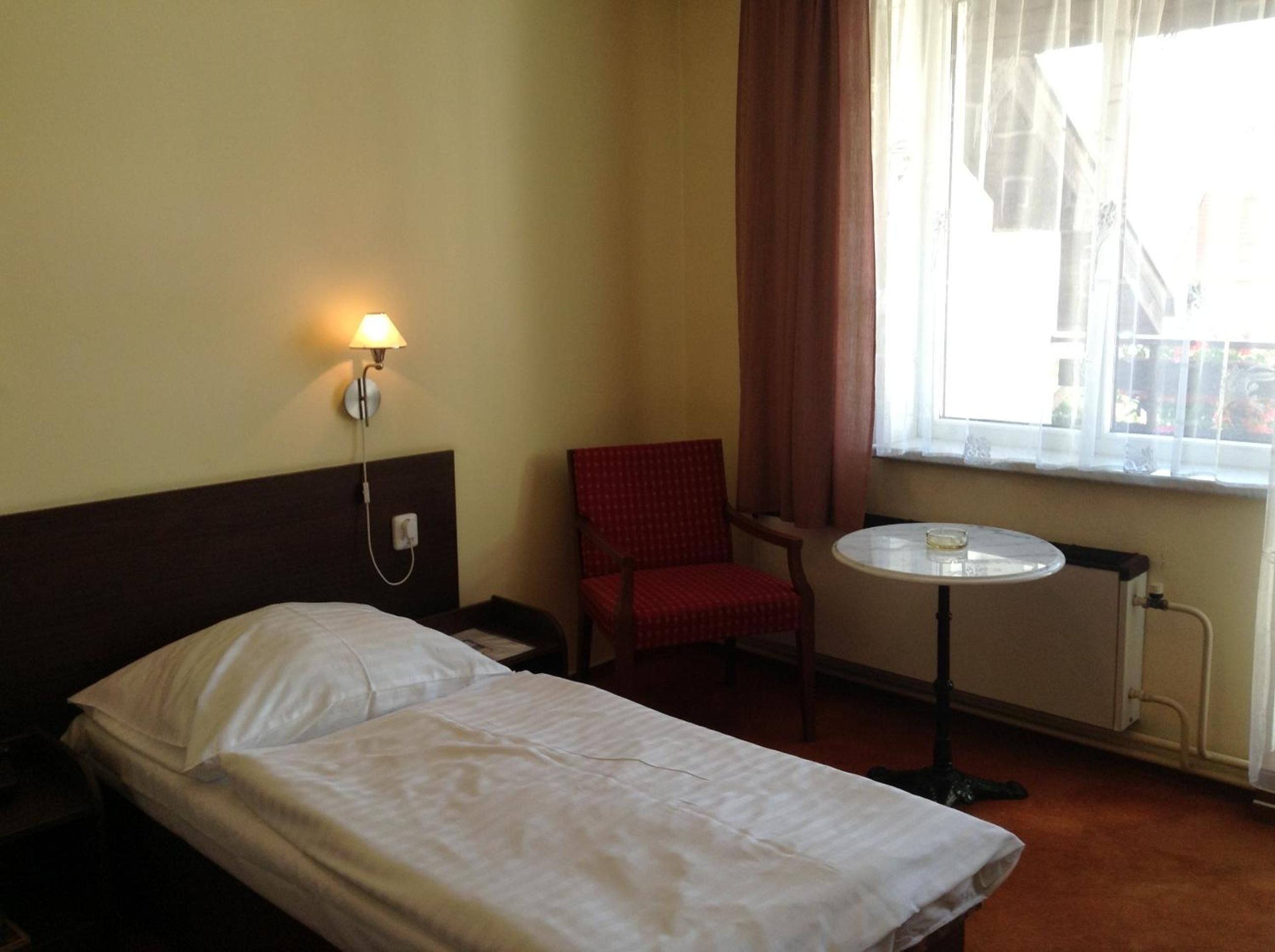 Una habitación de hotel con una cama individual, una silla, una mesita y una ventana con cortinas.