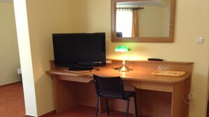 A hotel room with a bed, a desk with a TV, a chair, and a lamp. - Hotel York (Plzen)