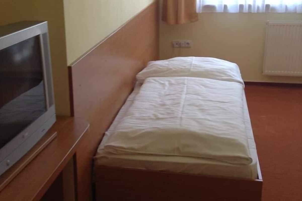 A small room with a wooden bed, a television on a stand, and a window with curtains.