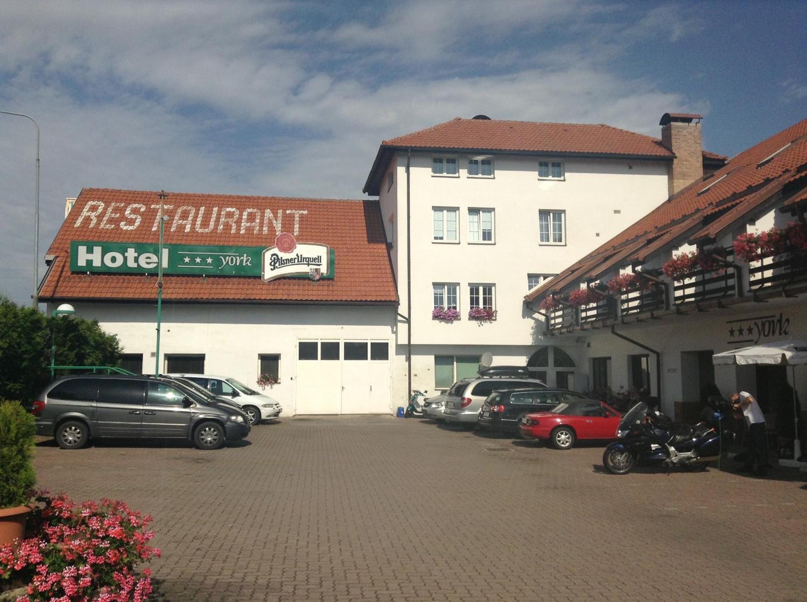 Un edificio con un letrero de restaurante y hotel. Hay coches estacionados y una motocicleta adelante.