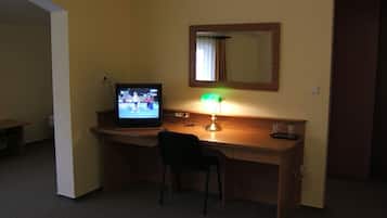A hotel room with a desk, a chair, a television, and a lamp.