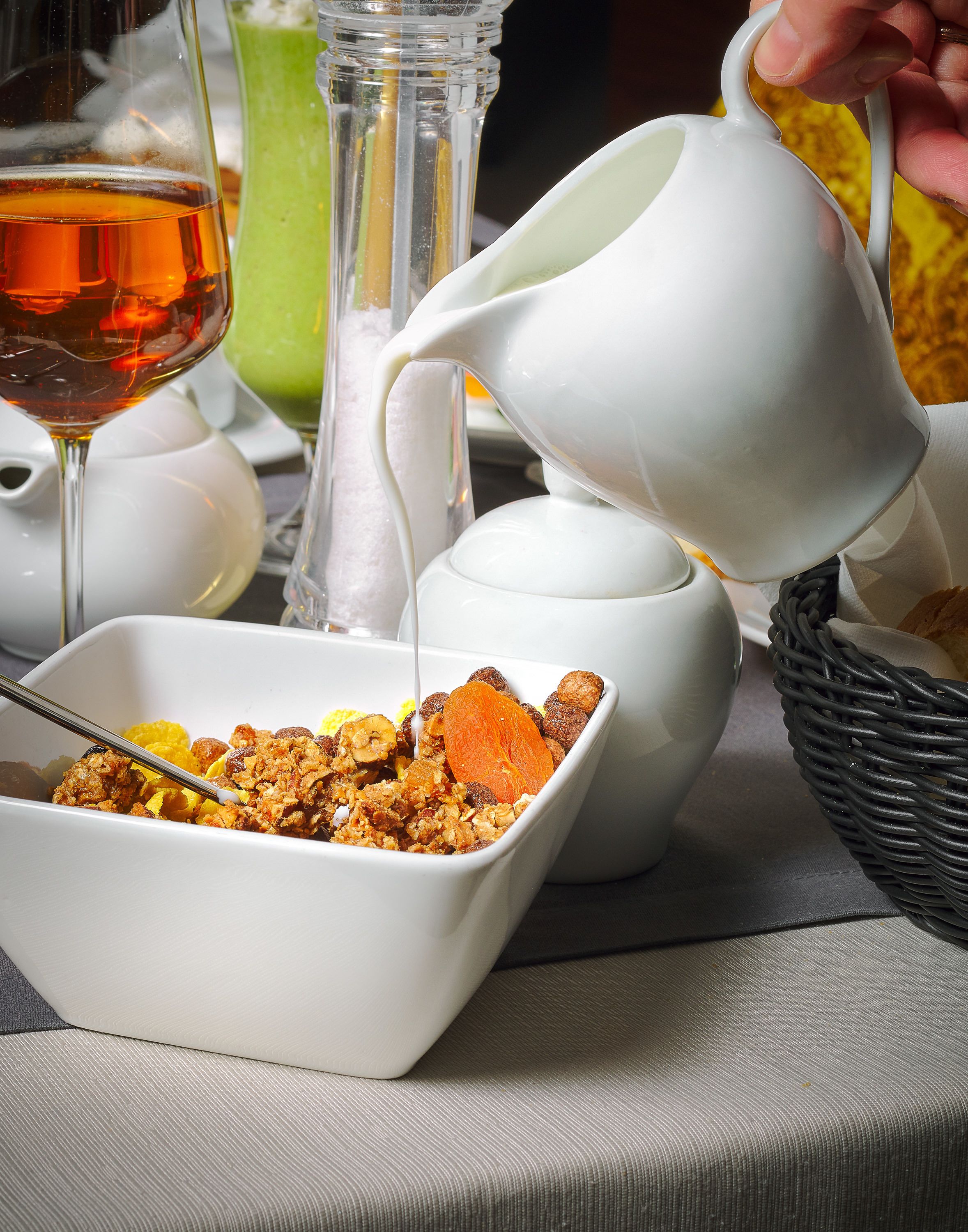 Un desayuno con un tazón de cereal, un vaso de jugo de naranja y una jarrón sirviendo leche.