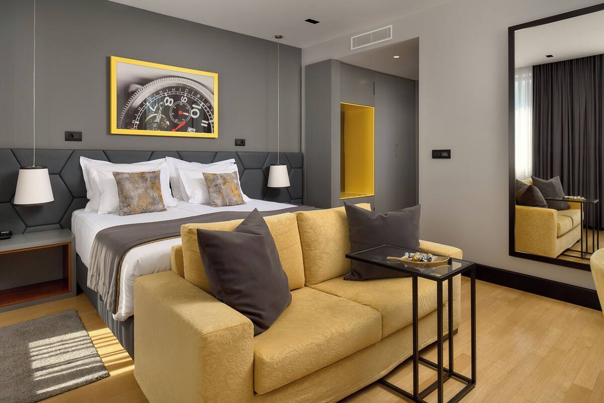 A modern hotel room with a bed, a sofa, a small table, and a large mirror.