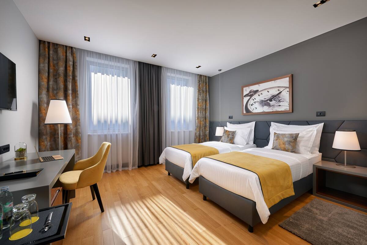 A hotel room with two beds, a desk, a chair, and a TV.