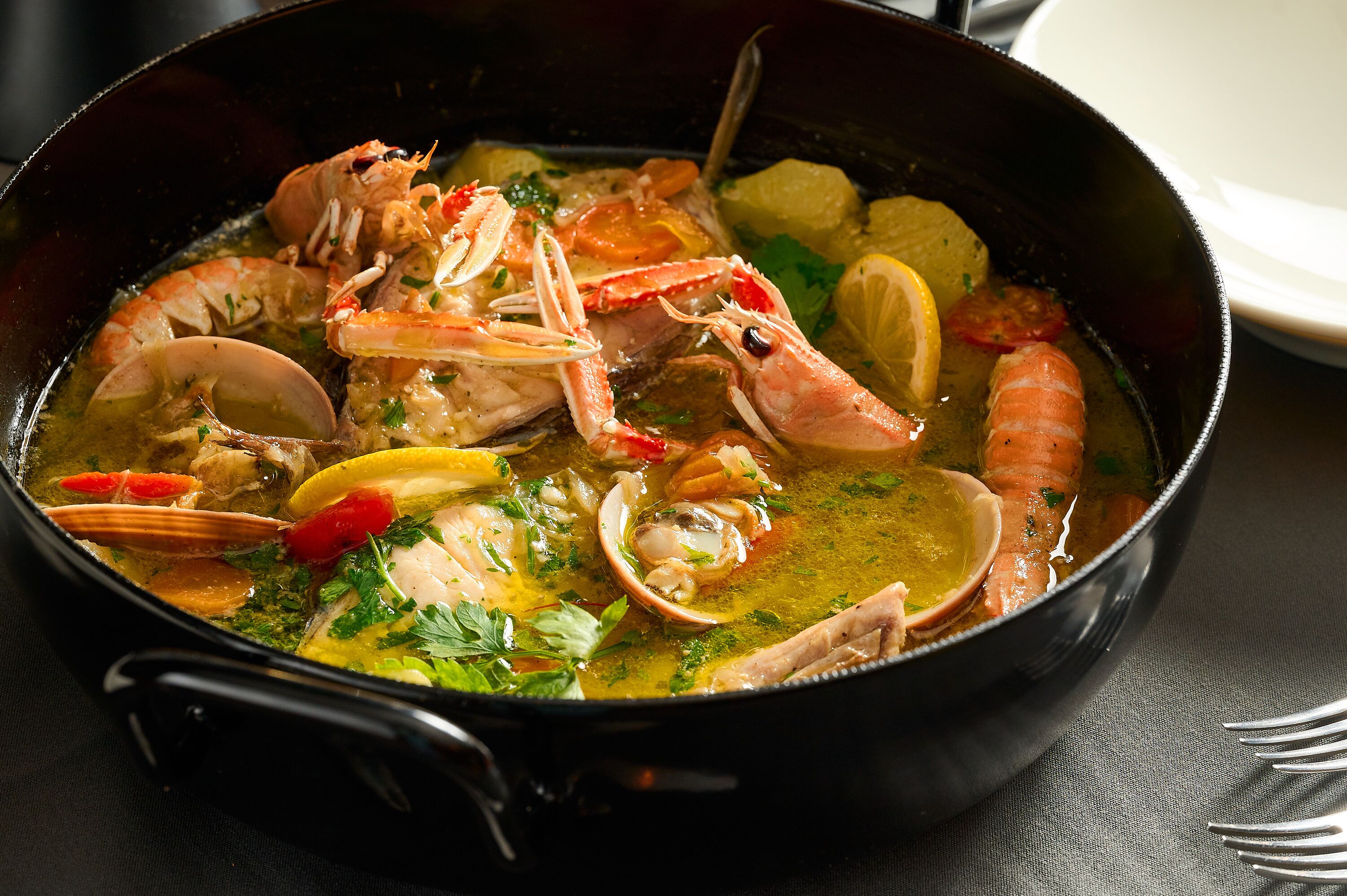 Un guiso de mariscos en una olla negra, con diversos mariscos y verduras.