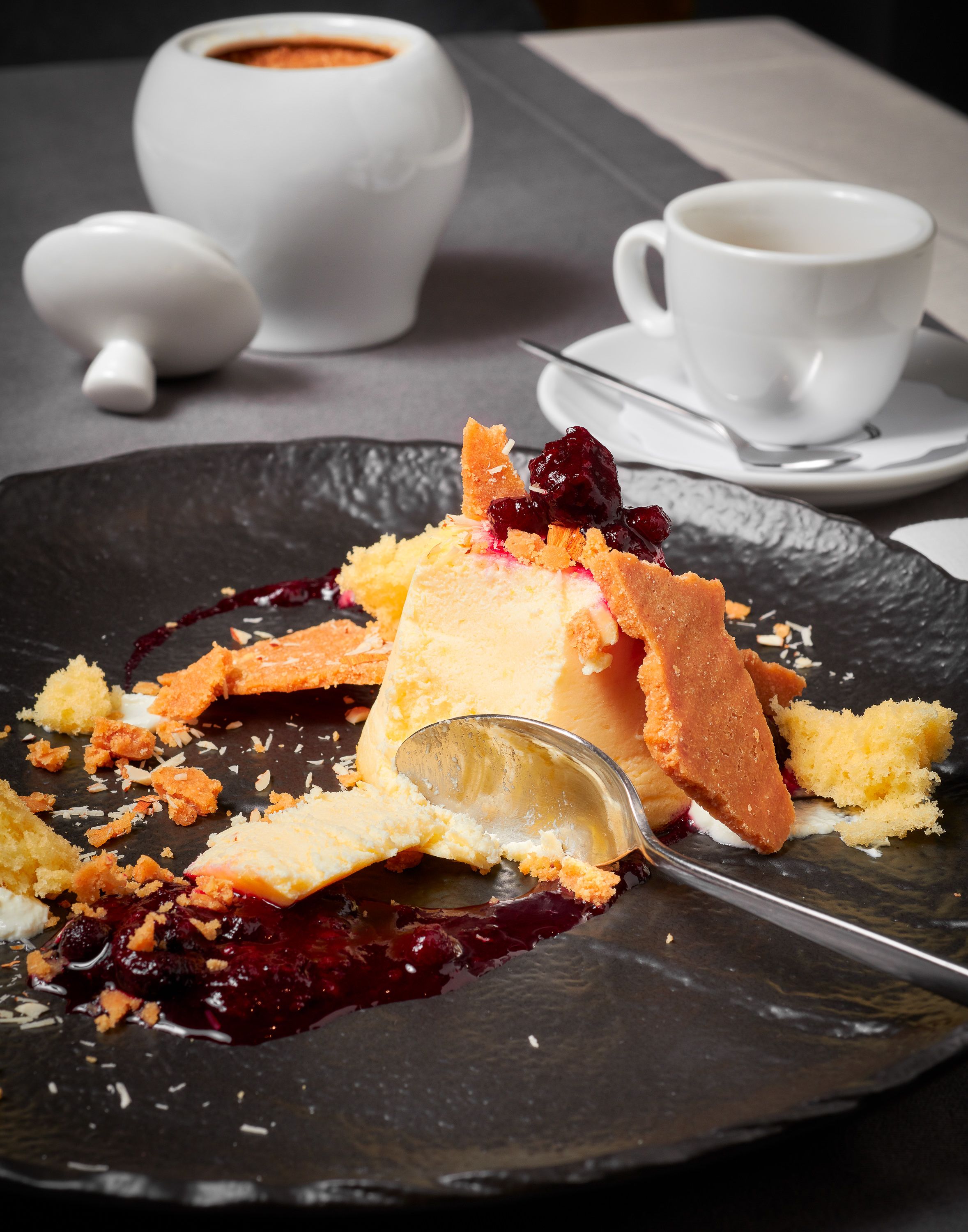 A dessert plate with a scoop of ice cream and fruit pieces on a dark plate.