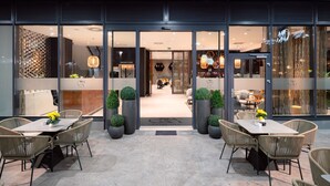 An outdoor seating area with tables and chairs, a reception desk, and a view into the interior of the hotel. - Sia Split Hotel (Split)
