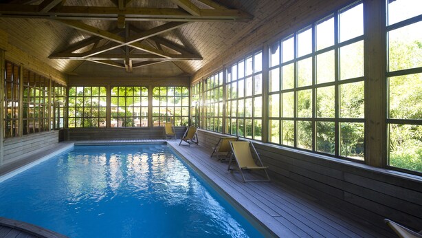 An indoor swimming pool with wooden deck, large windows, and sun loungers. - Hôtel le Pré Serroux (Champagney)
