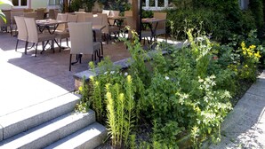 An outdoor patio with tables and chairs under a canopy, surrounded by lush greenery and a stone staircase. - Hôtel le Pré Serroux (Champagney)