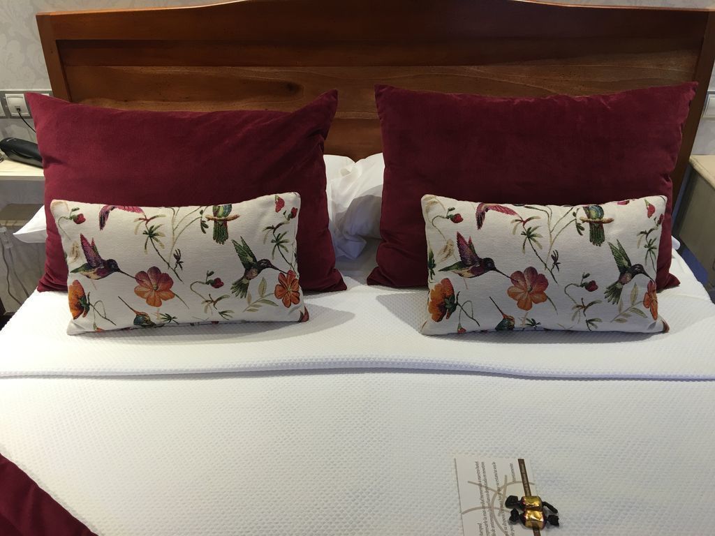 Una cama con dos almohadas, una con estampado floral y la otra lisa, además de un adorno sobre la cama.