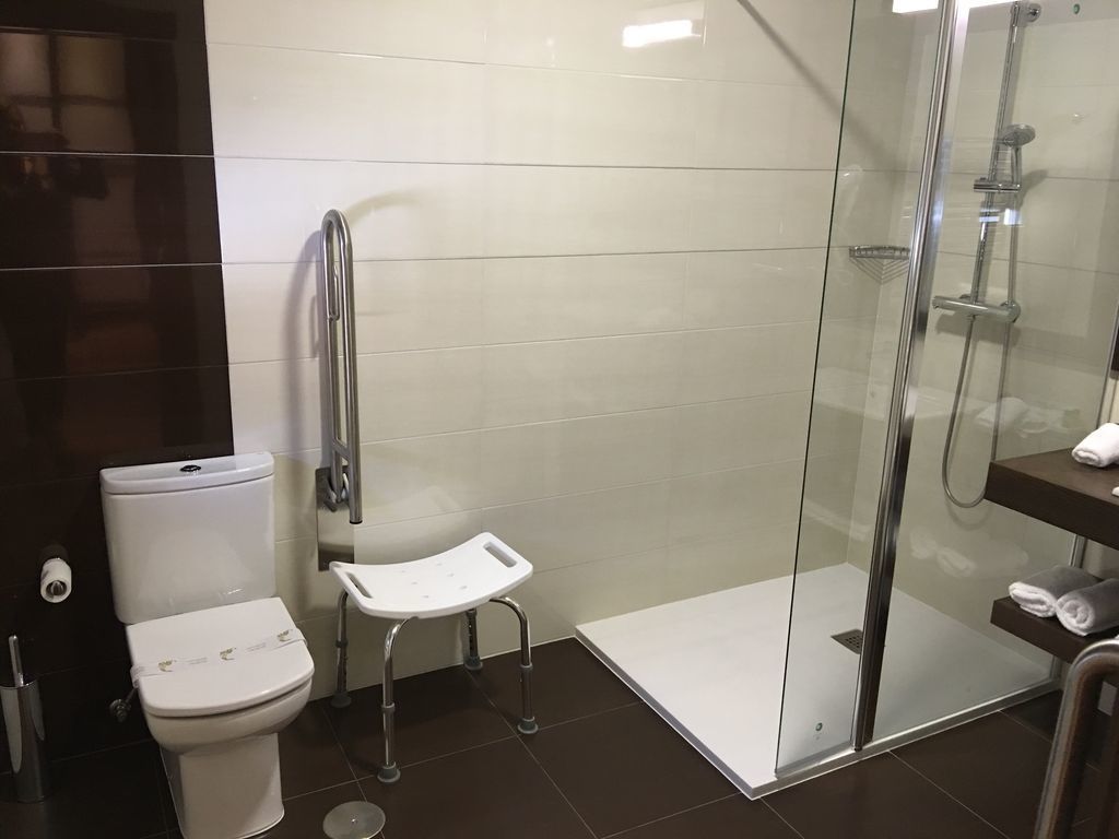 Un baño moderno con inodoro, ducha con puerta de cristal y un pequeño banco blanco.