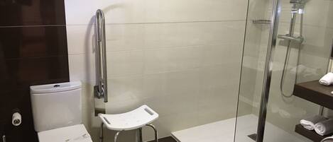 Un baño moderno con inodoro, ducha con puerta de cristal y un pequeño banco blanco.