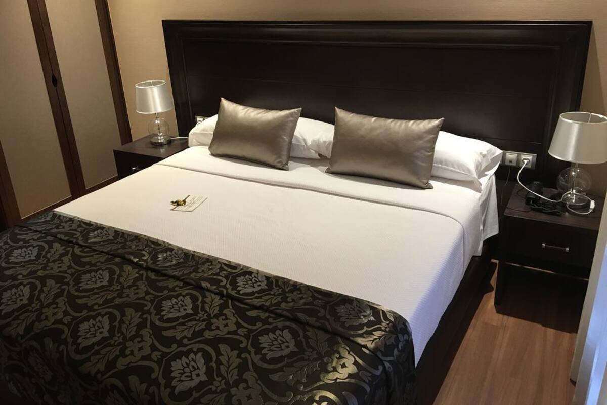 A neatly made bed with a patterned bedspread, two pillows, and a bedside table with a lamp.
