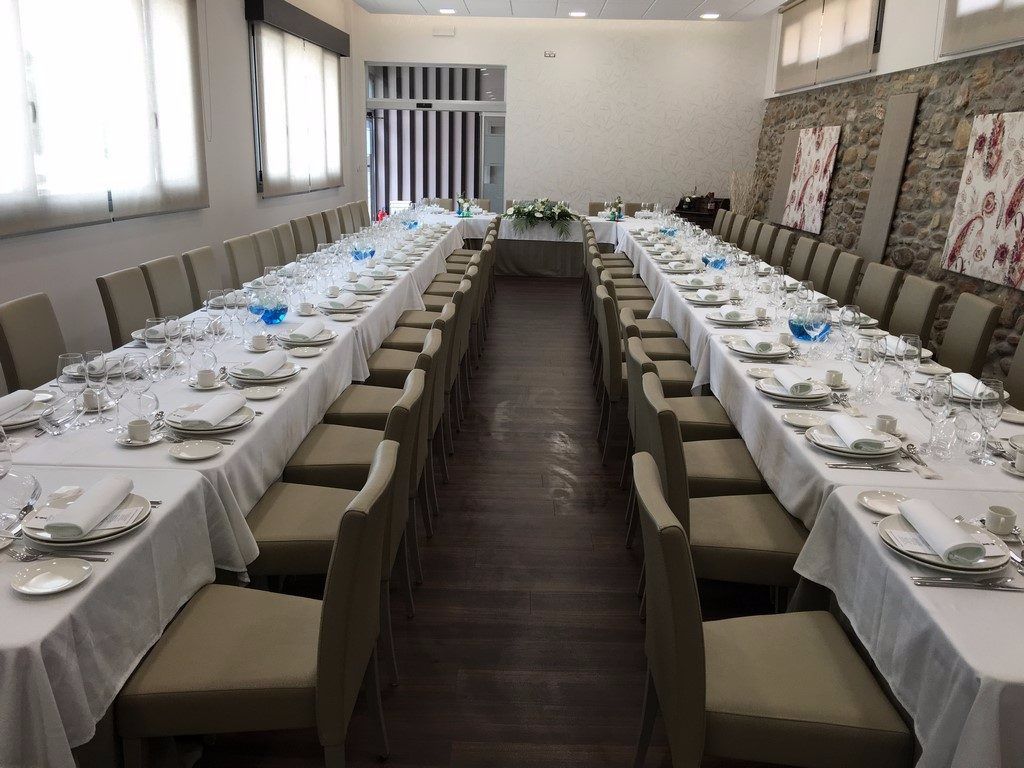 A long dining table set for a formal event with multiple chairs, white tablecloths, and a central floral arrangement.