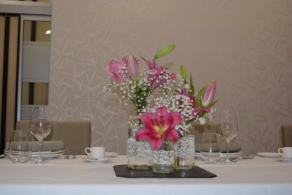 A dining table set with clear glassware and a centerpiece of pink lilies and baby's breath in glass vases.