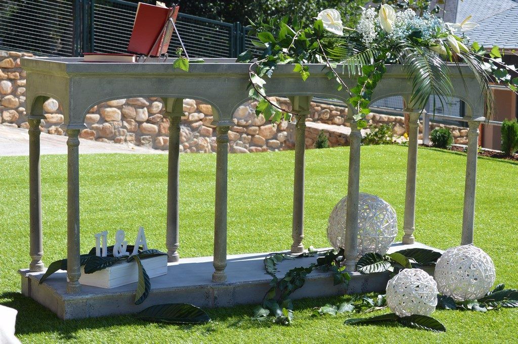 A stone bench with a book and a red book on top, surrounded by greenery and decorative spheres.