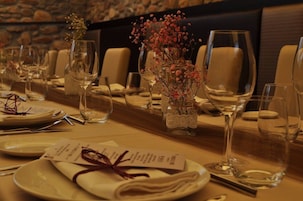 Una mesa de comedor elegantemente dispuesta, con copas de vino, platos y un centro de mesa con flores secas.