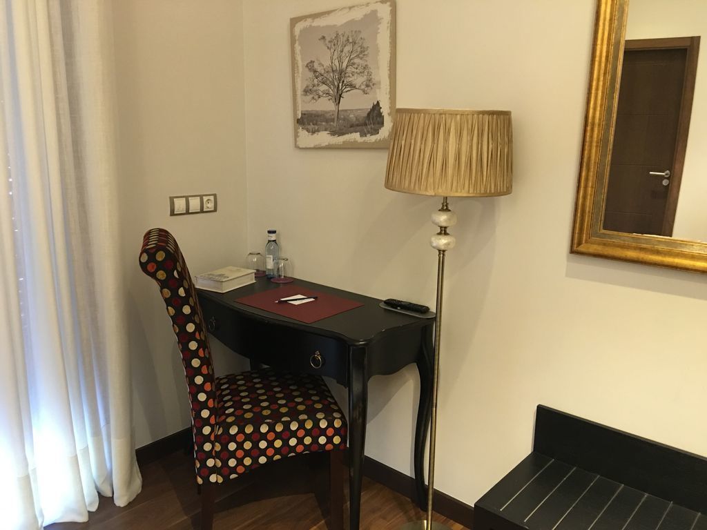 Una habitación de hotel con escritorio, silla, lámpara y una puerta.