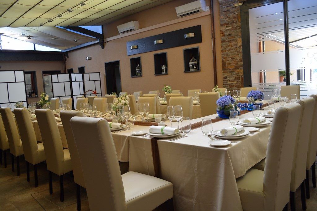A conference room with long tables set for a formal event, featuring beige chairs and white tablecloths.