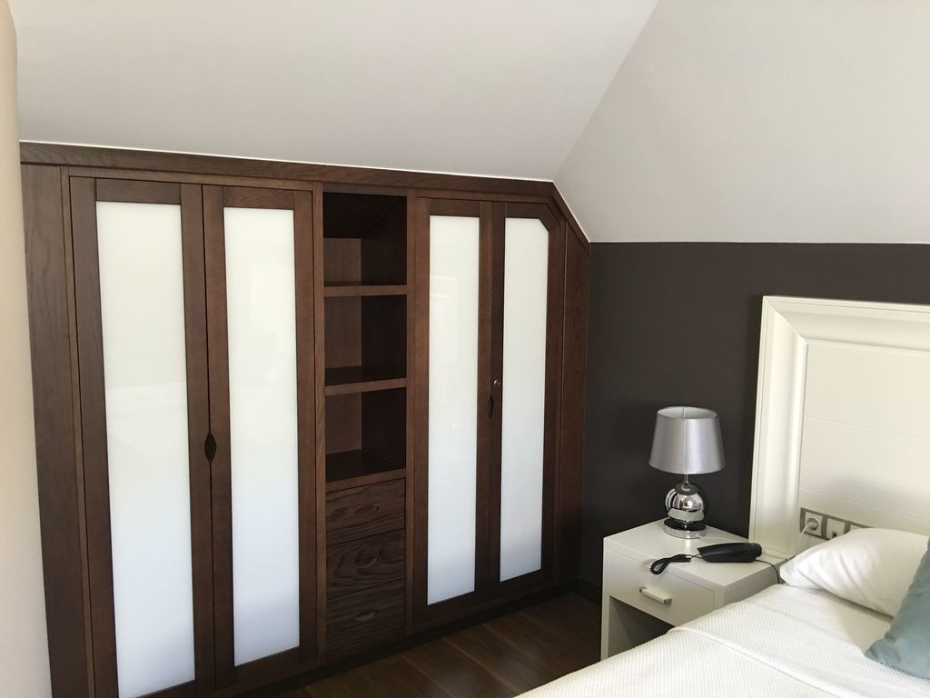 A bedroom with a wardrobe, a bedside table with a lamp, and a bed.