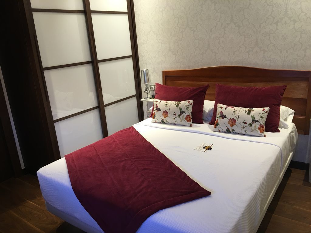 A neatly made bed with a red throw blanket, floral pillows, and a wooden headboard.