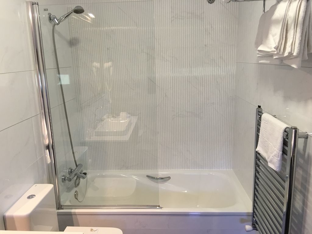 A modern bathroom with a glass-enclosed shower, a bathtub, and a towel rack.