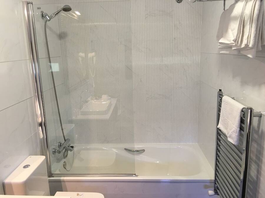 Un baño moderno con ducha envuelta en vidrio, bañera y perchero.