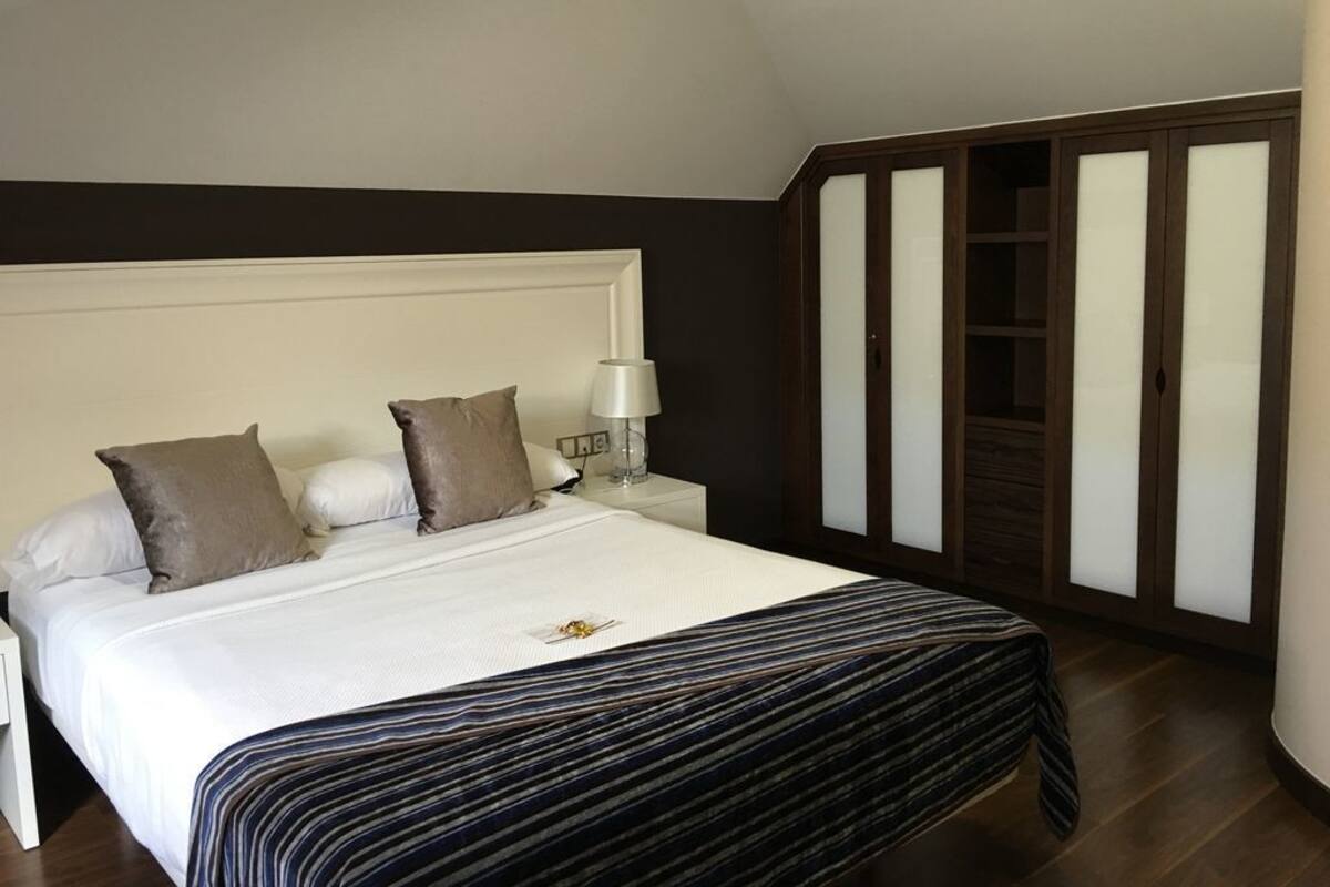 A bedroom with a large bed, a nightstand, a lamp, and a wardrobe with frosted glass doors.