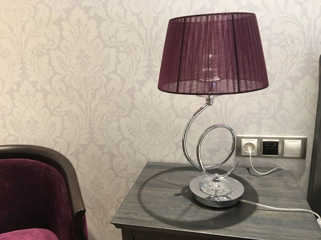 A modern lamp with a metallic base and a purple shade on a wooden nightstand.
