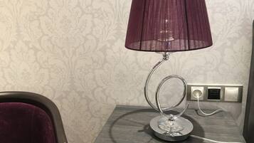 A modern lamp with a metallic base and a purple shade on a wooden nightstand.