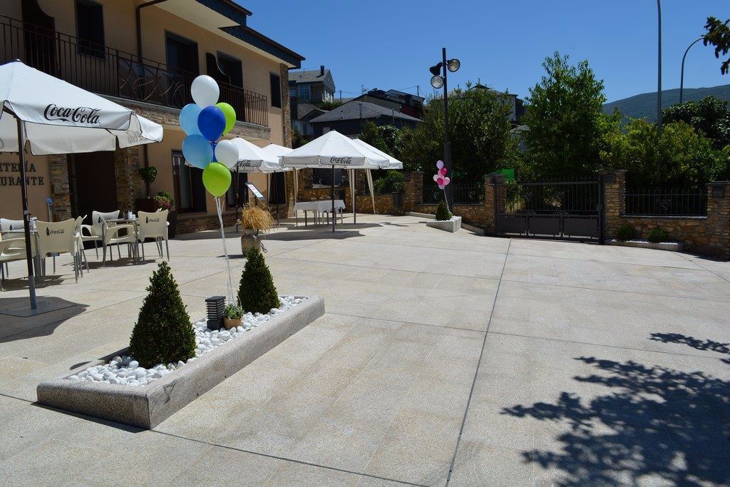 Un área de patio al aire libre con sombrillas blancas de Coca-Cola, arreglos de asientos y una jardinera de piedra con árboles pequeños.