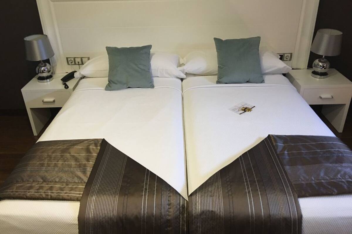 A double bed with two pillows, a nightstand with a lamp, and a small decorative item on the bed.