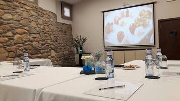 Un salón de conferencias con pared de piedra, una pantalla de proyector, botellas de agua y un mantel blanco.