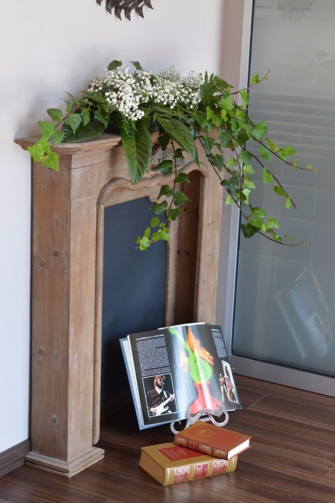 Una estantería de madera con libros y una revista, una planta decorativa y un marco de pared.