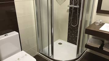 Une salle de bain moderne avec une douche à parois de verre, des toilettes blanches et un sol carrelé foncé.
