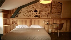 A bedroom with a large bed, wooden walls, a sloped ceiling, a desk, and a chair. - Hôtel Le Quatorze (Figeac)