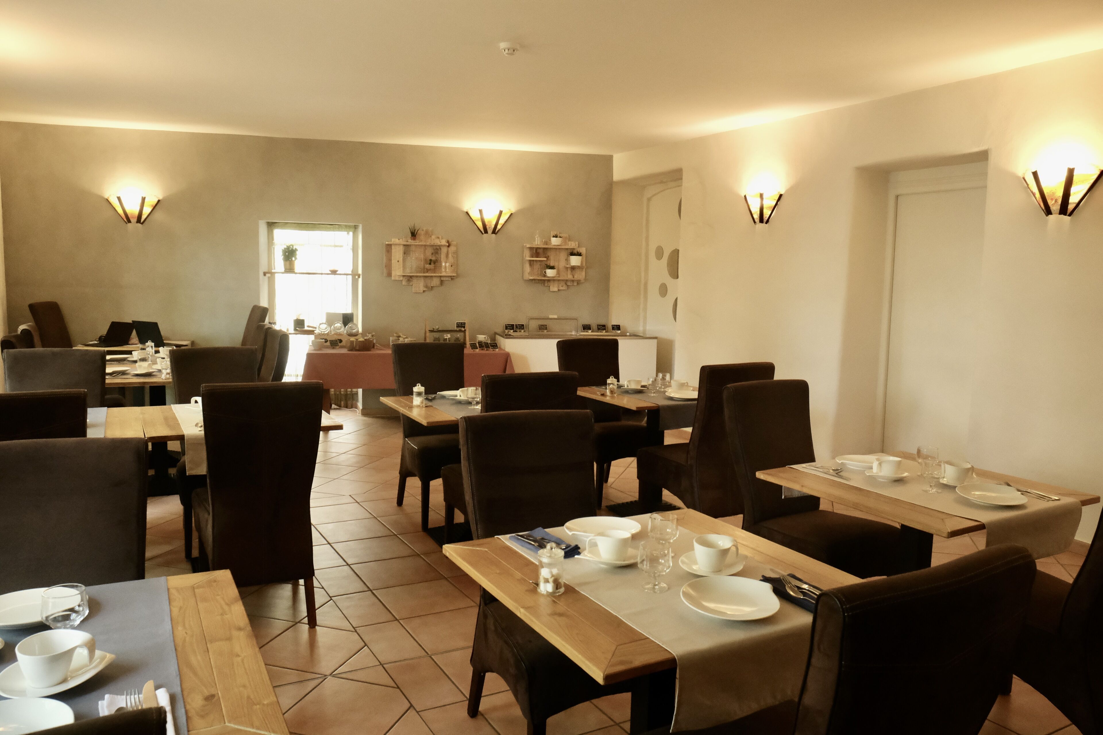 A dining area with multiple tables and chairs, equipped with table settings and wall-mounted light fixtures.