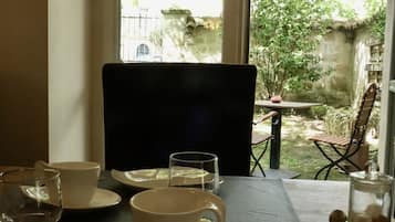 Una mesa de comedor dispuesta con platos, tazas y cubiertos, con vistas a un jardín a través de una ventana.