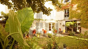 A courtyard with potted plants, outdoor furniture, and a building with shutters. - Hôtel Le Quatorze (Figeac)