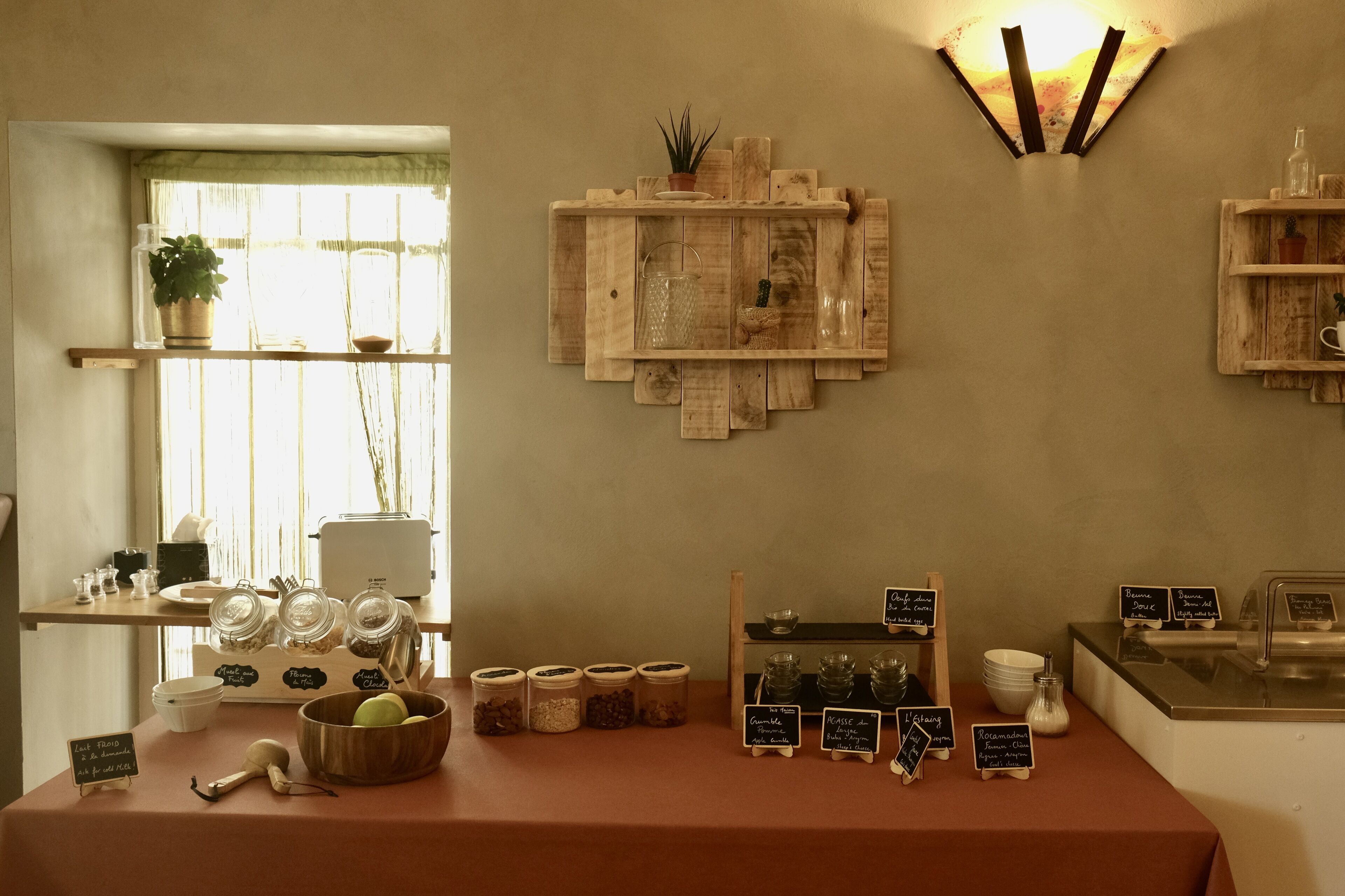 Um café com prateleiras de madeira exibindo potes e um quadro negro com o menu.