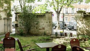 Une terrasse avec des sièges extérieurs, un mur en pierre et une vue sur la rue.