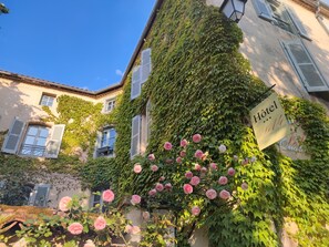 A hotel facade with ivy-covered walls, a sign indicating it is a hotel, and blooming pink roses. - Hôtel Le Quatorze (Figeac)