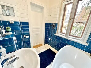 A bathroom with a white sink, a white bathtub, and a window with a view of buildings outside.