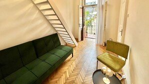 A room with a green sofa, a small table with a chair, a staircase, and a balcony with plants. - Apartment Siroka 14 (Prague)