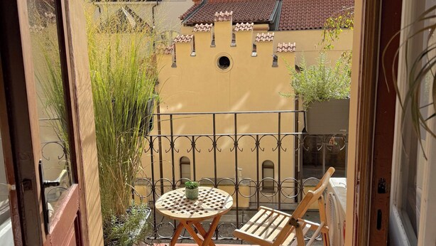 A balcony with a small table and chair, a potted plant, and a view of buildings with red-tiled roofs. - Apartment Siroka 14 (Prague)