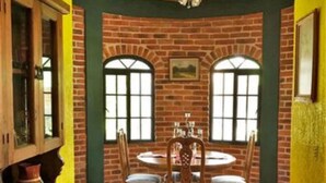 A dining area with a brick wall, two arched windows, a wooden table with chairs, and a tiled floor. - Villa Meli 2 by Kivoya (Jocotepec)